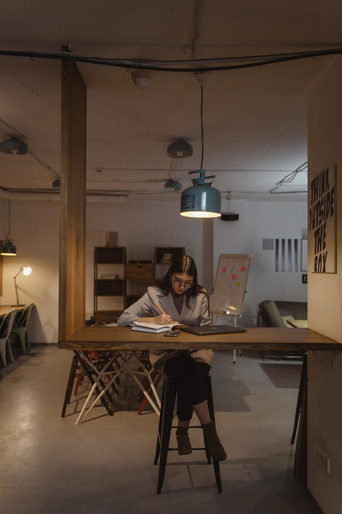 Businesswoman writing notes under pendant lamp in a stylish modern office interior.